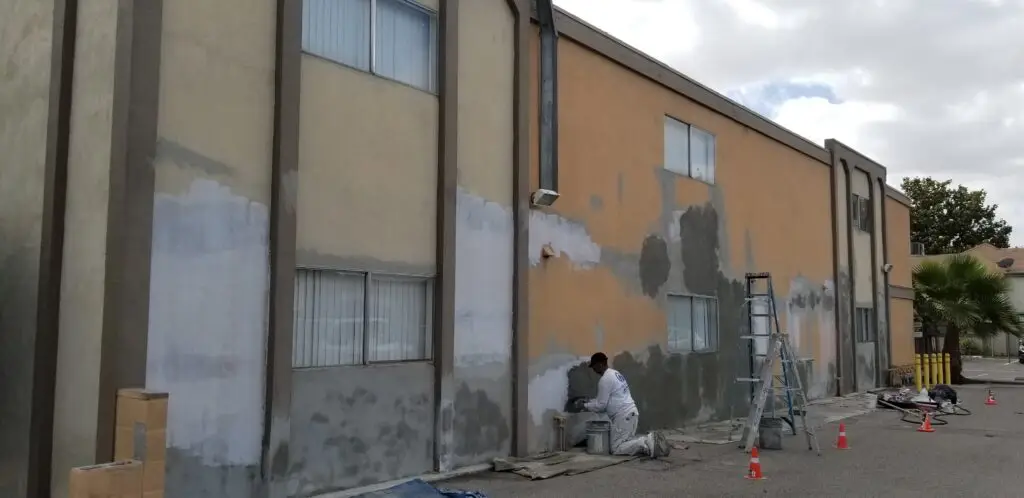 Commercial apartment building painter preparing stucco surfaces thoroughly for exterior painting, including cleaning and surface repairs.