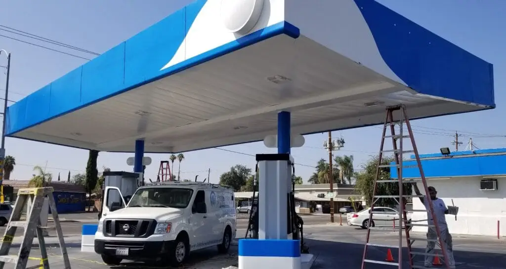 Commercial building painting of a gas station exterior overhead structure with John Hernandez Painting company vehicle.